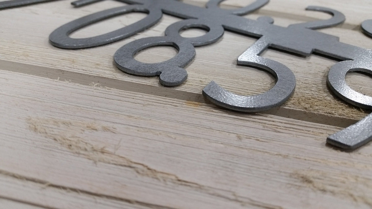 a close up of the metal GPS coordinate sign showing the cut quality and level of detail. the sign is finished in a textured hammered black paint.