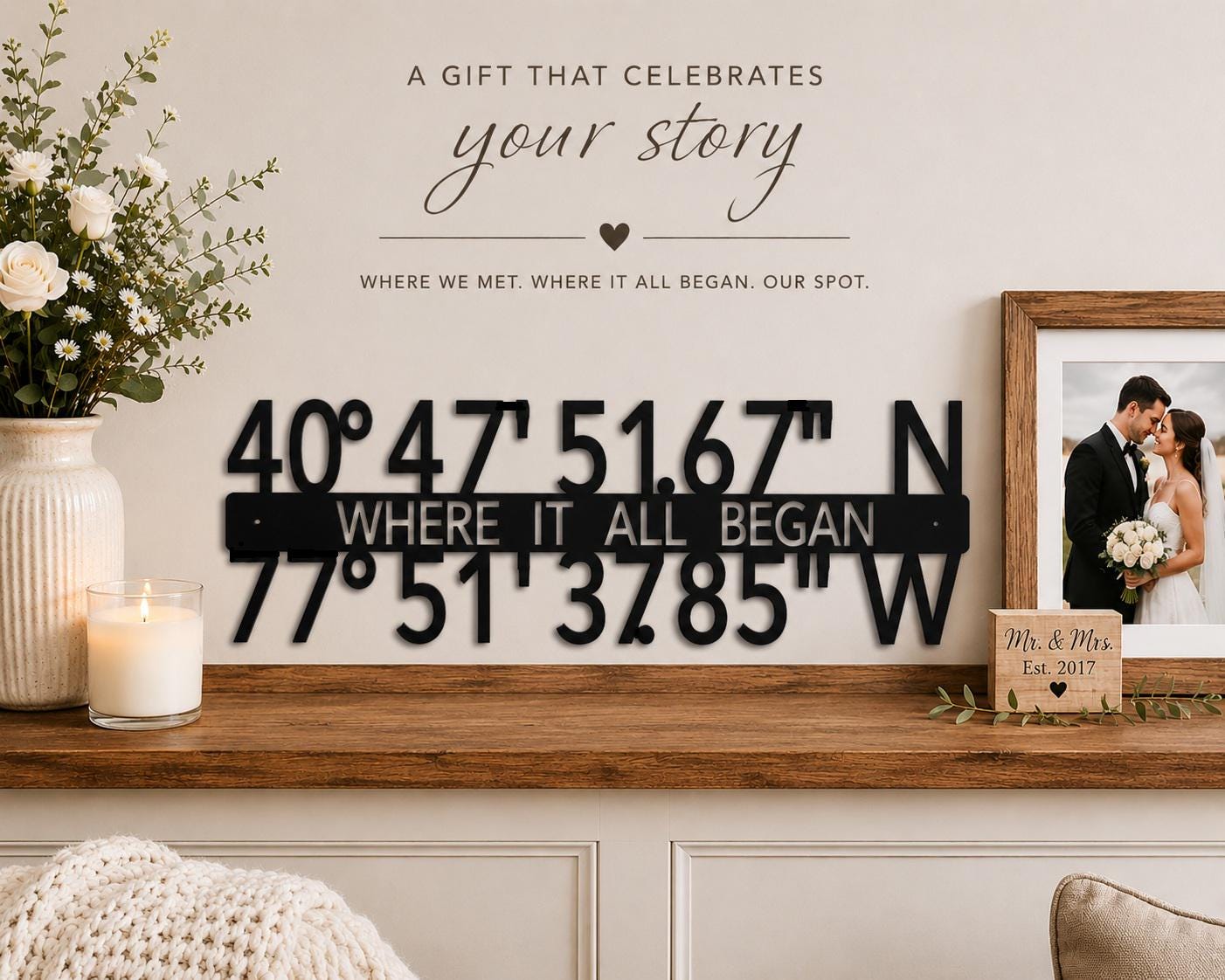 May include: A black metal sign with coordinates and the text "WHERE IT ALL BEGAN." The sign is displayed on a wooden shelf, alongside a framed photo and a decorative vase with flowers. The text "A GIFT THAT CELEBRATES your story" is above the sign.